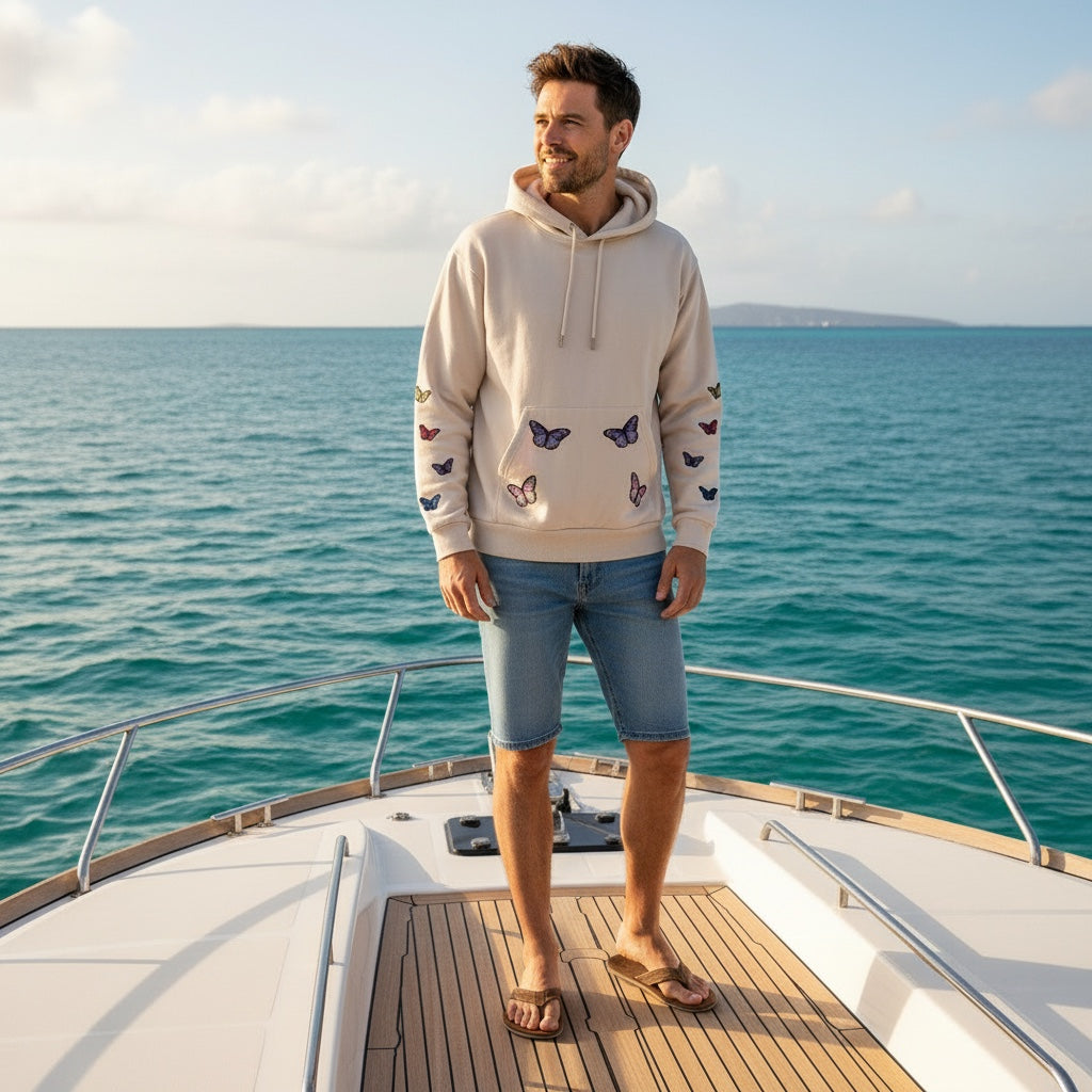 A Brand Called California unisex beige cotton hoodie with embroidered butterflies on the front and sleeves, worn by a man on a beach.
